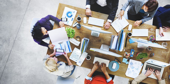 Vogelperspektive auf eine Gruppe gemeinsam arbeitender Menschen an einem Schreibtisch