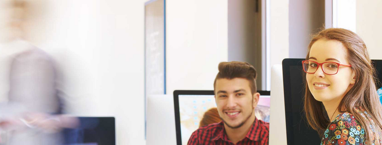 Zwei Studierende vor Bildschirmen lächeln in die Kamera
