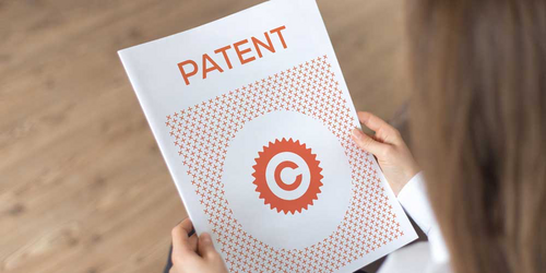 Frau hält weißes Papier mit roter Aufschrift: Patent
