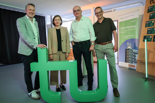 4 Personen vor großem TU-Logo