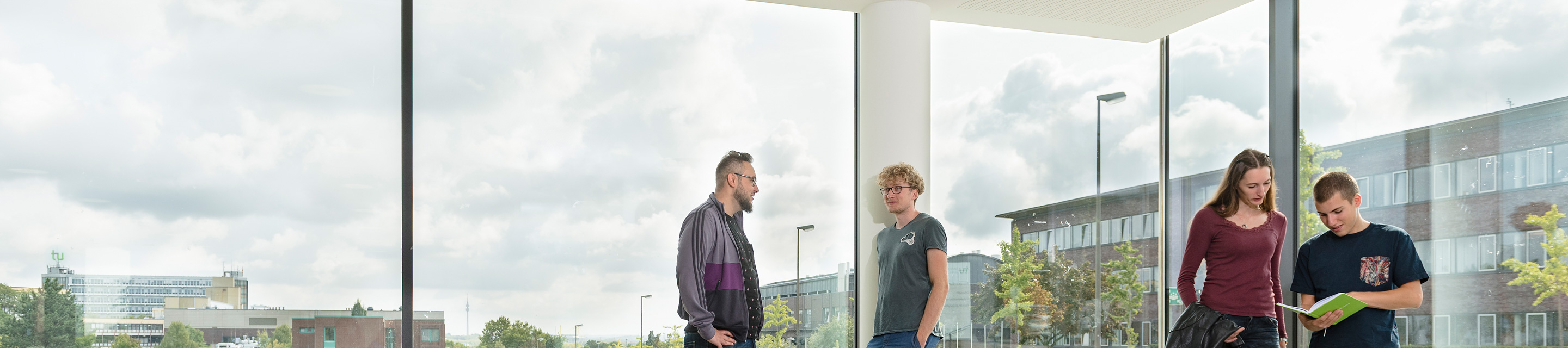 Studenten in Gesprächssituationen vor einer Fensterfront