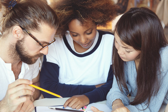 Three students put their heads together over documents.