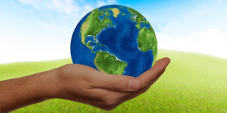 One hand holds a globe against the background of a green meadow with a blue sky.