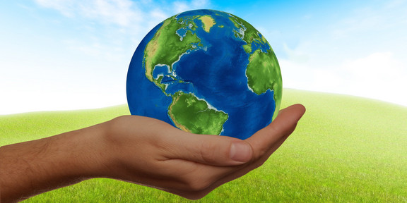 One hand holds a globe against the background of a green meadow with a blue sky.