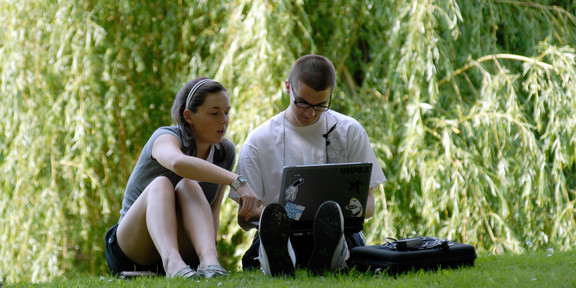 Eine Studentin und ein Student beim gemeinsamen Lernen mit Laptop auf einer Wiese im Sommer